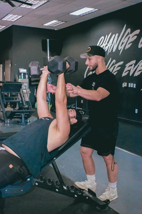 Coach assisting a client with a dumbbell press in a private gym